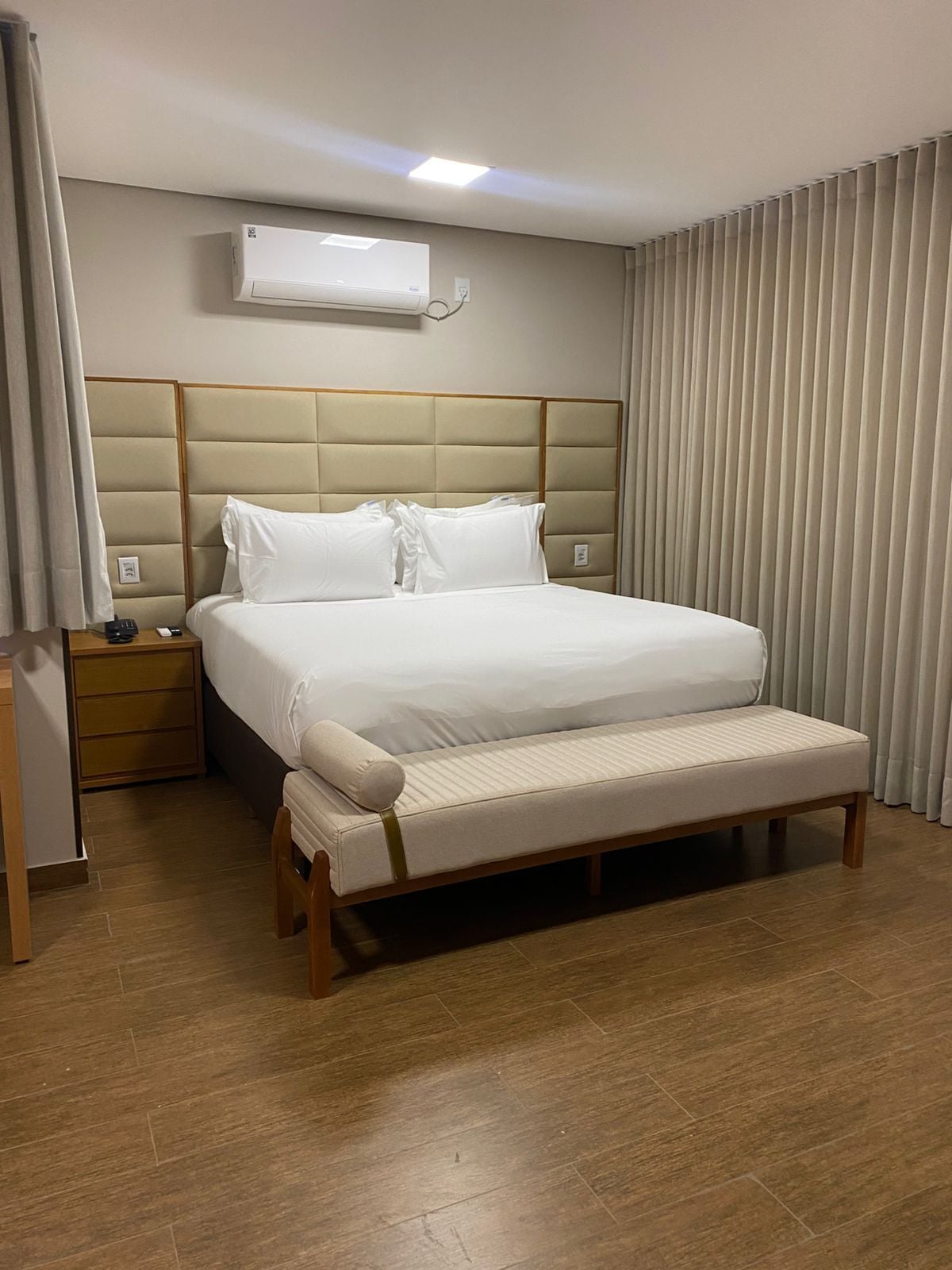 Una habitación de hotel con cama, mesita de noche y unidad de aire acondicionado.