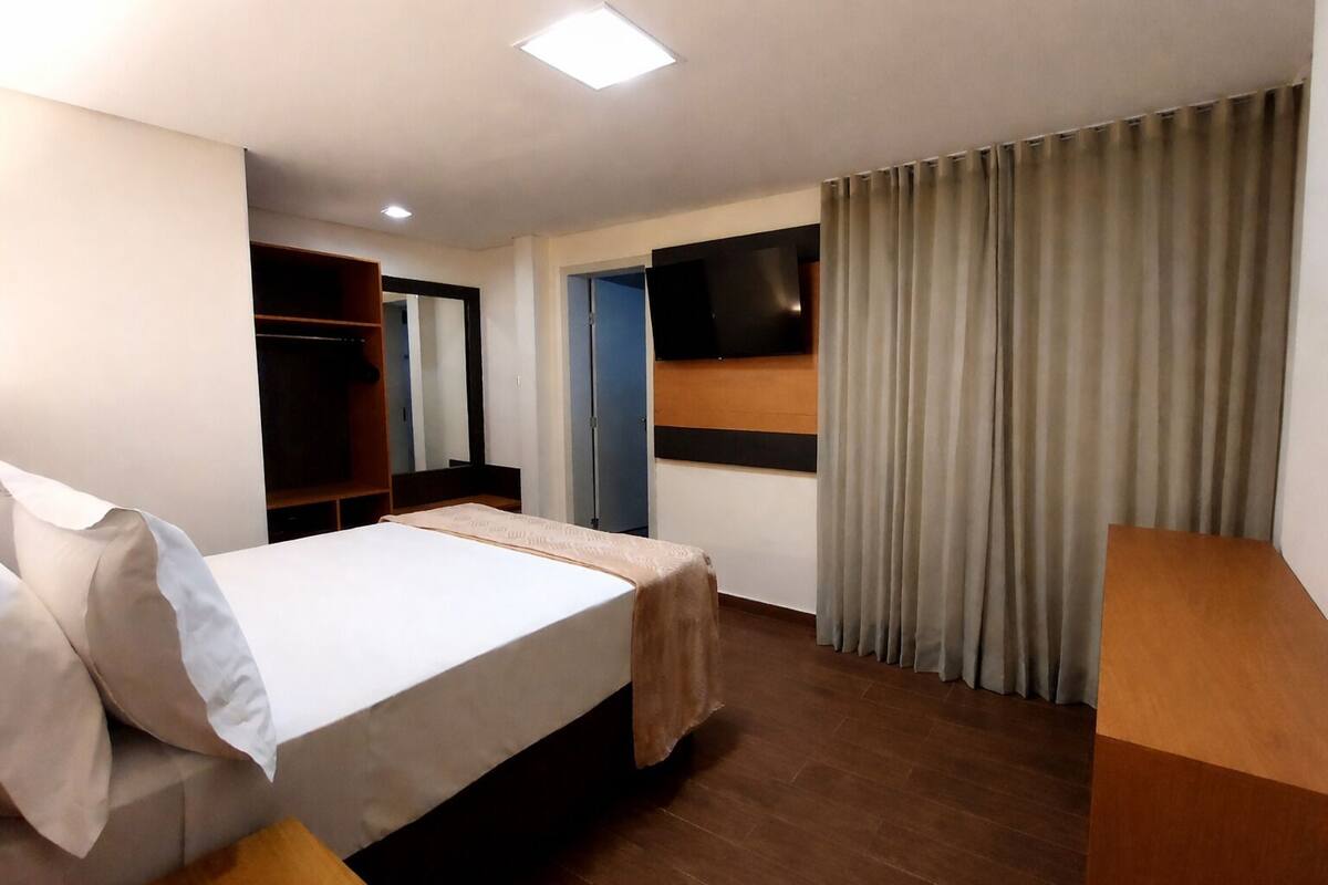 Une chambre d’hôtel avec un lit, une armoire, un téléviseur fixé au mur et un rideau.
