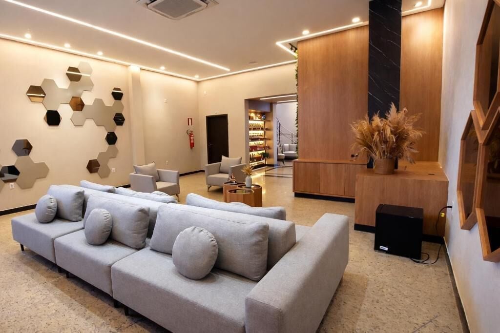 A modern hotel lobby with a grey sofa, a wooden reception desk, and a wall with hexagonal mirrors.