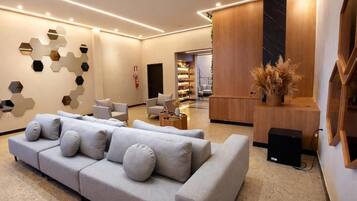 A modern hotel lobby with a grey sofa, a wooden reception desk, and a wall with hexagonal mirrors.