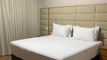 Une chambre d’hôtel avec un grand lit, une table de chevet en bois, un climatiseur fixé au mur et une fenêtre avec des rideaux.