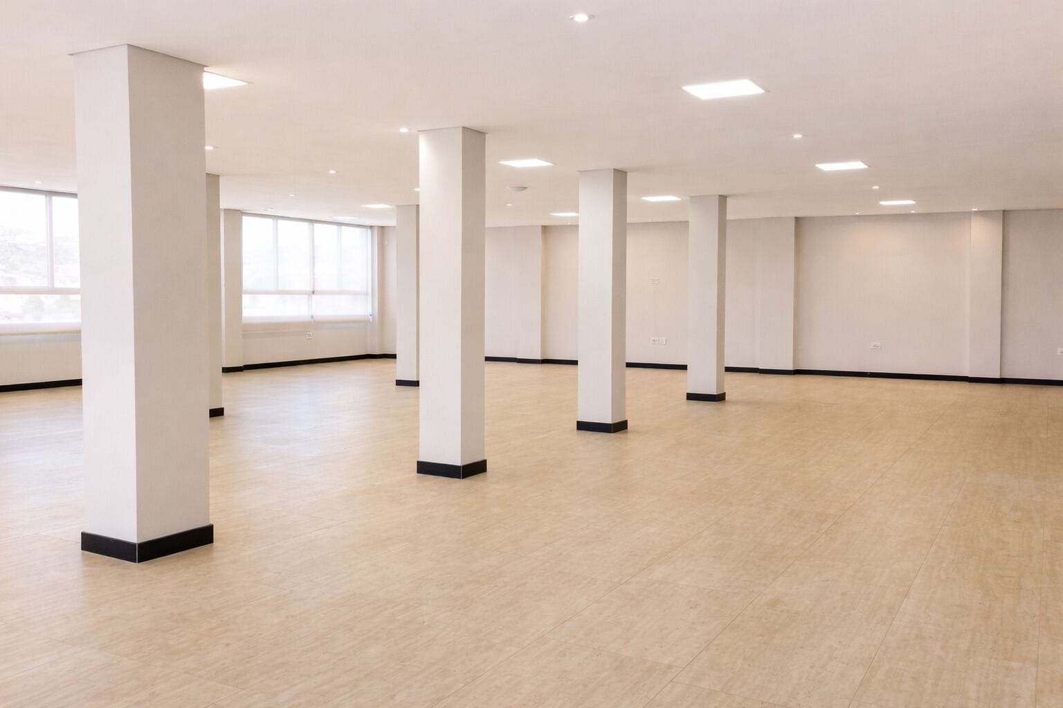 A spacious room with a high ceiling, white pillars, and a light wooden floor.