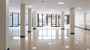 A spacious, well-lit indoor area with a polished floor, large windows, and a view of an outdoor swimming pool. - HOTEL OURO MEL (Santa Bárbara)