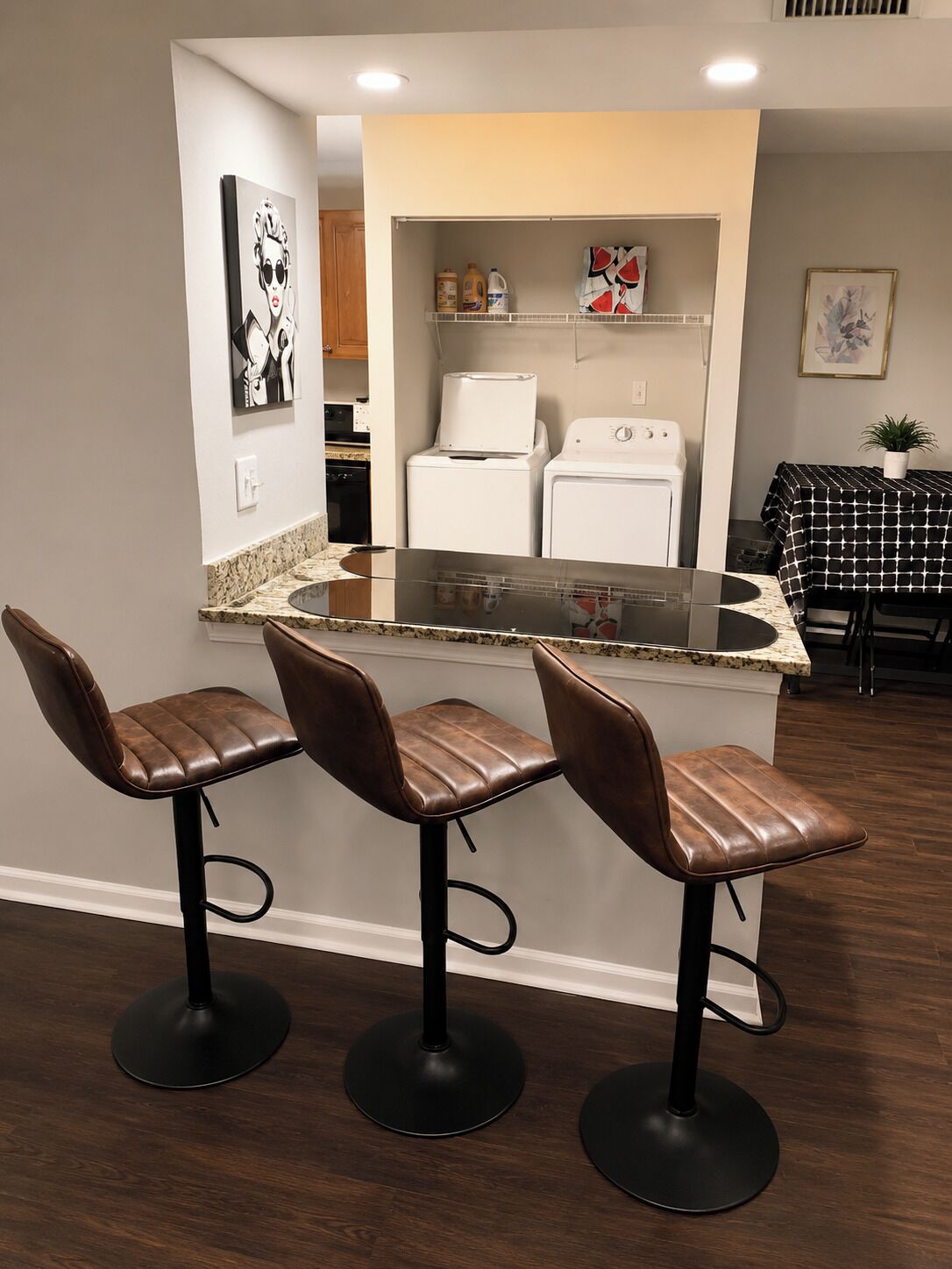 A kitchen with a central island, three bar stools, and a dining table with a patterned tablecloth.