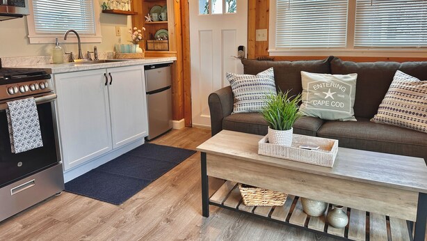A cozy kitchen with wooden cabinets, a stove, and a sink. There is a wooden dining table with a plant and a tray.
