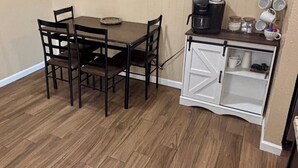 Un'area pranzo di dimensioni ridotte con tavolo e sedie, una macchina per il caffè e un mobiletto con ripiani.