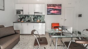 A modern kitchen with white cabinets, a microwave, and a sink. There is a glass table with a laptop and a cup. A brown leather chair is in the foreground. - Apartment with balcony near Maradona Stadium (Napoli)