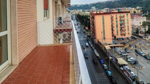 A balcony with a red-tiled floor overlooking a busy street with cars and buildings. - Apartment with balcony near Maradona Stadium (Napoli)