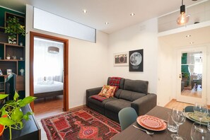 A modern living room with a grey sofa, a dining table set with plates and glasses, a patterned rug, and a bookshelf with plants. - Green Living Apartment (Milan)
