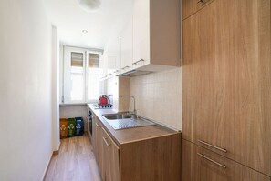 A narrow kitchen with wooden cabinets, a stainless steel sink, and a window providing natural light. - Green Living Apartment (Milan)