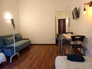 Ein gemütlicher Wohnraum mit Sofa, kleinem Tisch, Esstisch mit Stühlen und einem an der Wand befestigten Fernseher.
