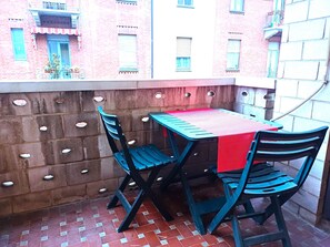Ein kleiner Balkon mit Tisch und zwei Stühlen, einer roten Tischdecke und einer Ziegelwand mit Verzierungen.