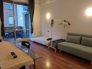 Ein kleiner, gut beleuchteter Raum mit einem Glastisch, einer Couch, einem Bett und einer Stehlampe.