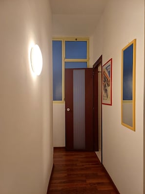 Ein Flur mit Holzboden, einer Tür mit vertikaler Jalousie und einer Wandleuchte.