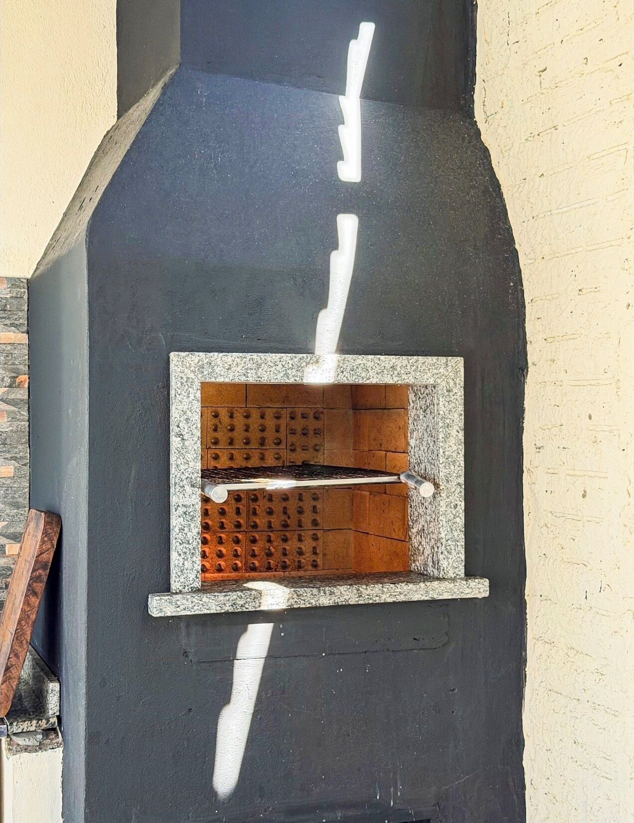 Un horno de ladrillo con una rejilla metálica en su interior, apoyado contra una pared.