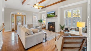 A spacious living room with a fireplace, wooden beams, a television, and a dining area with a table and chairs.