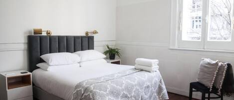 Ein ordentlich eingerichtetes Schlafzimmer mit einem Bett, Nachttischen, einem Stuhl und einem Fenster.