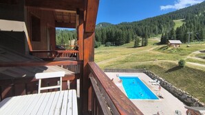 Eine Holzhütte mit einem Balkon mit Blick auf ein Schwimmbecken und eine Berglandschaft.