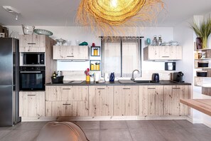 A modern kitchen with wooden cabinets, a built-in microwave, and a large island with a sink. - La Vista - Climatisé, vue mer (Grosseto-Prugna)