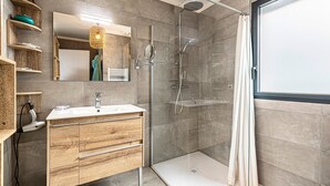 Un bagno moderno con cabina doccia in vetro, mobile lavabo in legno e uno specchio grande.