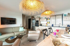 A modern living room with a sofa, a coffee table, and a dining area with a table and chairs. There is a kitchen area with cabinets and a refrigerator. - La Vista - Climatisé, vue mer (Grosseto-Prugna)