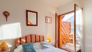A bedroom with a bed, a nightstand with a lamp, a mirror, and a picture on the wall. There is a window with a view of a mountain. - Le Parc Neige - Vue Montagne (Briancon)
