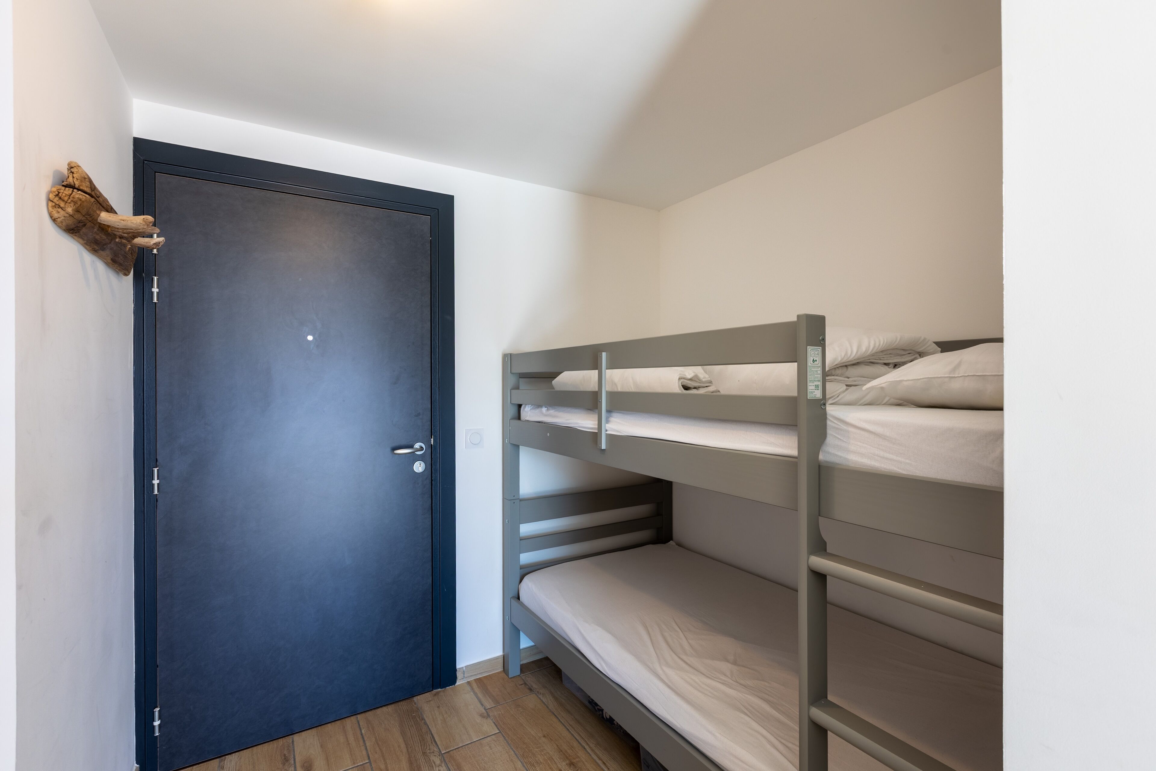 A room with a bunk bed, a dark door, and a small wall-mounted shelf.