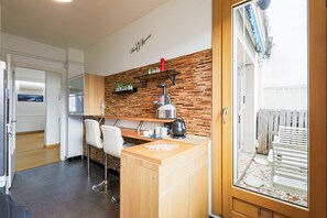 A compact kitchen with a wooden countertop, a coffee machine, and a shelf with kitchen items. - Le Berthelot - Terrasse avec Vue Montagne (Grenoble)