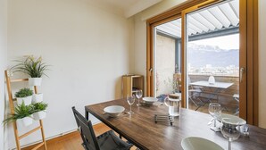 Zona pranzo con tavolo in legno, sedie e vista sulle montagne tramite una porta in vetro.