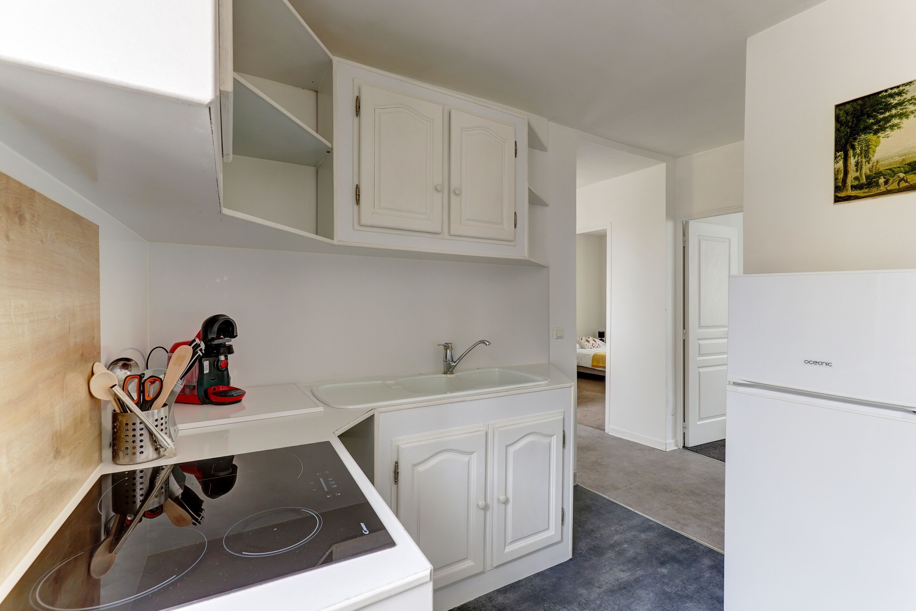 Una cocina compacta con armarios blancos, un lavamanos integrado y una cafetera.