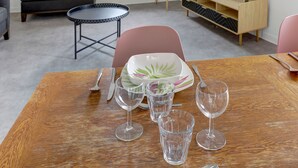 Ein Essbereich mit einem Holztisch, vier Weingläsern, einem Teller mit grüner Blattform und einem kleinen runden Tisch mit schwarzem Metallgestell.