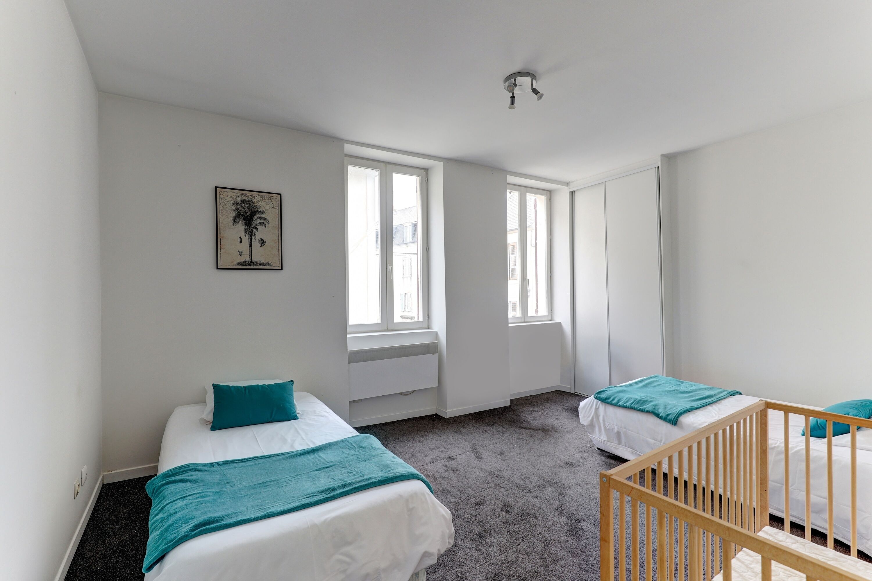 Una habitación con dos camas, una cuna y ventanas amplias.