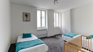 Ein Zimmer mit zwei Betten, einem Reisebett und großen Fenstern.