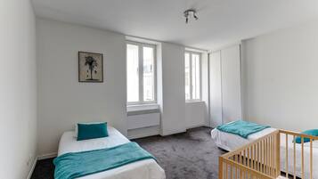 Una habitación con dos camas, una cuna y ventanas amplias.