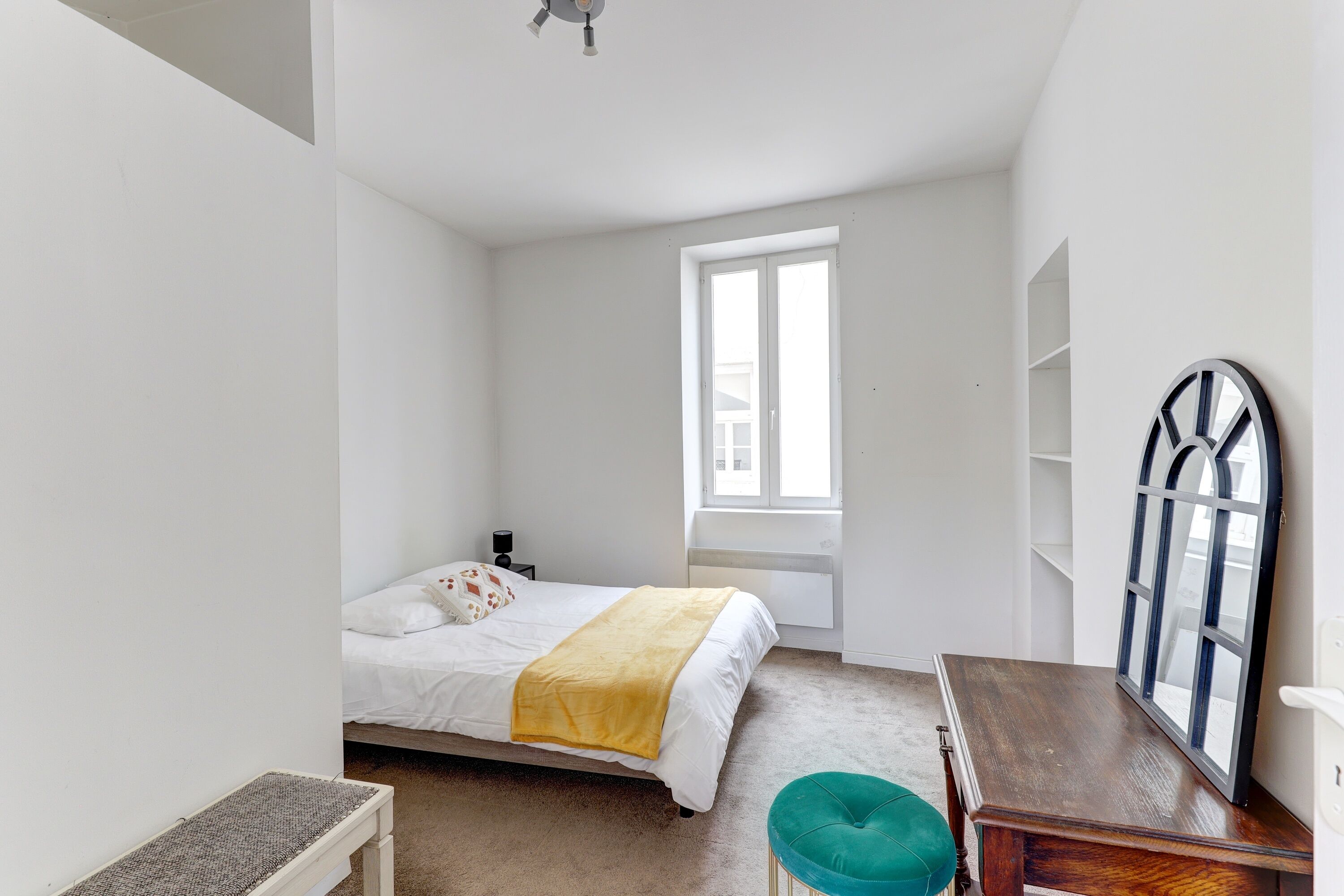 Une chambre à coucher avec un lit, une fenêtre, une table de chevet et un miroir.
