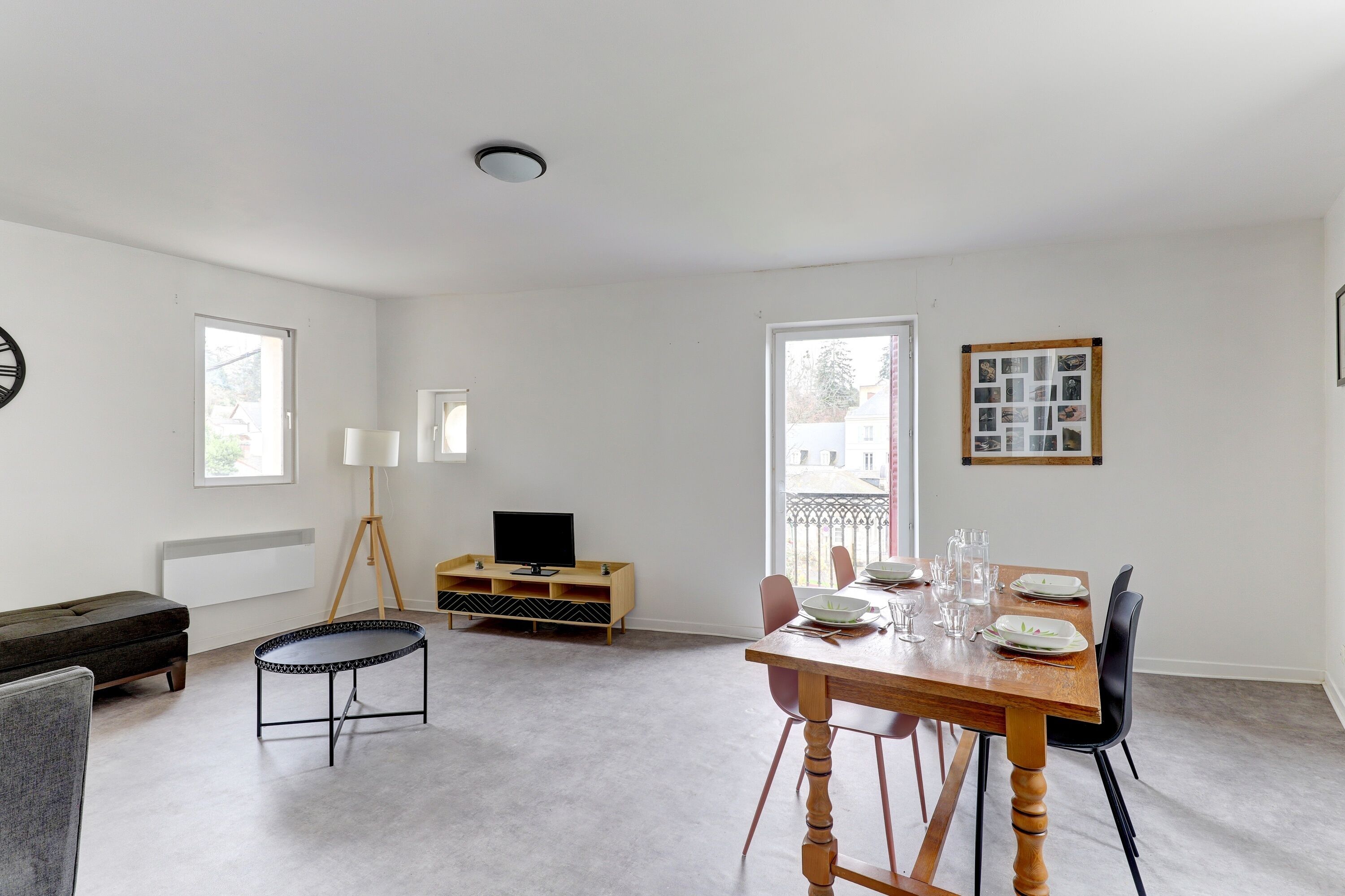 Una sala de estar moderna con una mesa de comedor preparada para cuatro personas, un sofá, una pequeña mesa de centro y un televisor sobre un mueble de madera.