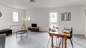 Ein modernes Wohnzimmer mit Esstisch für vier Personen, einer Couch, einem kleinen Couchtisch und einem Fernseher auf einem Holzständer.