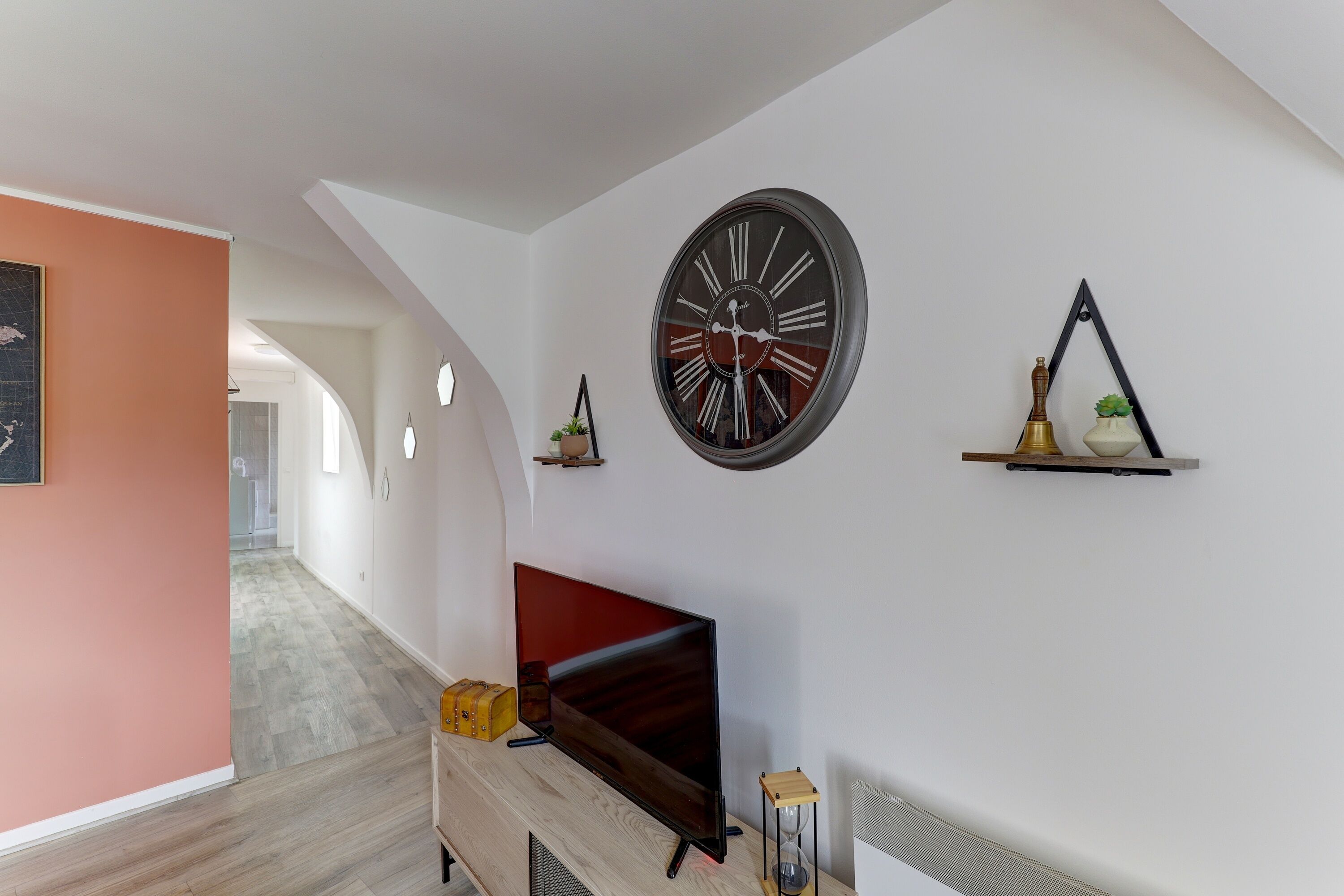Een moderne woonkamer met een flatscreen televisie, een grote wandklok en een minimalistische inrichting.