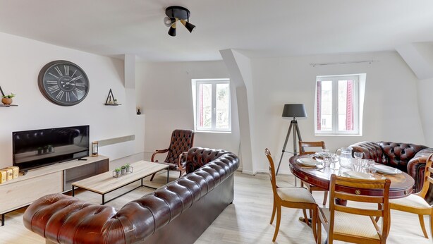 Un salon moderne avec un canapé en cuir, une table à manger pour quatre personnes et un téléviseur.