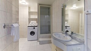 Une salle de bain moderne dotée d’un lave-linge intégré, d’une douche à parois de verre et d’un grand miroir.