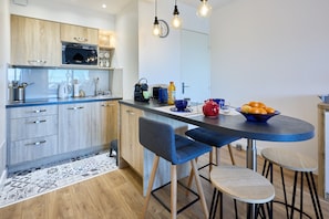 Une cuisine moderne avec des meubles en bois, un four à micro-ondes et un coin repas agrémenté de chaises et de tabourets bleus.