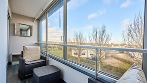 A balcony with wicker furniture, a cushioned bench, and a view of a residential area. - Les Camélias - 5min à pied du Port (Courseulles-sur-Mer)