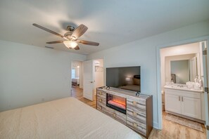 Ein Schlafzimmer mit Bett, Wandfernseher, Kamin und Deckenventilator.