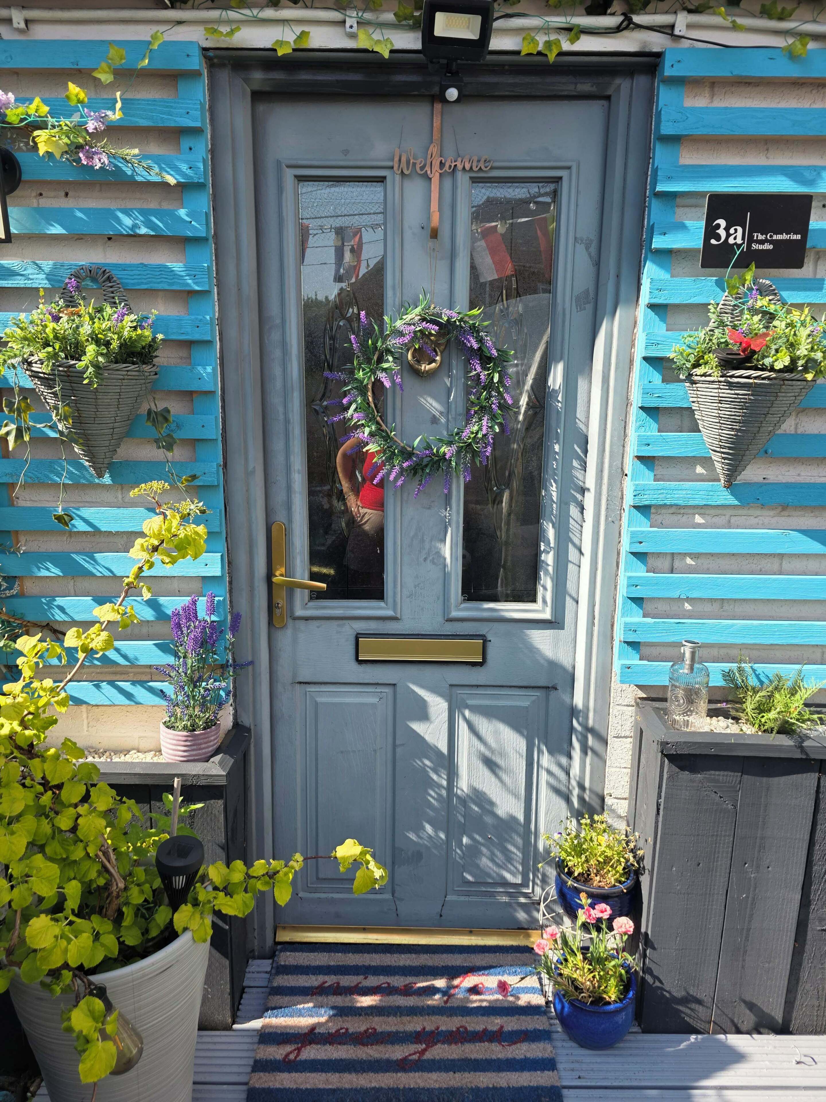 Une porte bleue ornée d’une pancarte de bienvenue, d ’une guirlande et de plantes en pot.