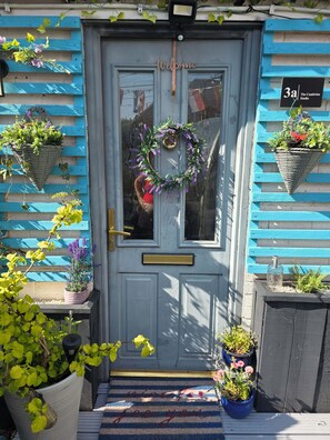 Una puerta azul con un letrero de bienvenida, una corona de laurel y plantas en macetas.