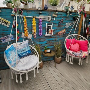Un espacio exterior acogedor con dos sillones colgantes y una pequeña mesa, decorado con objetos de viaje y plantas.