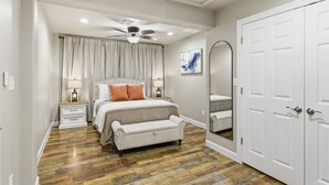 Ein Schlafzimmer mit einem Bett, Nachttischen, einer Bank, einem Deckenventilator, einem Spiegel und einem Kleiderschrank.