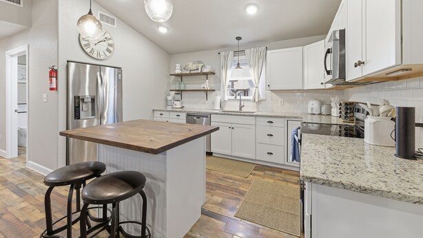 Eine moderne Küche mit weißen Schränken, Edelstahlgeräten und einer Holztheke mit Barhocker.