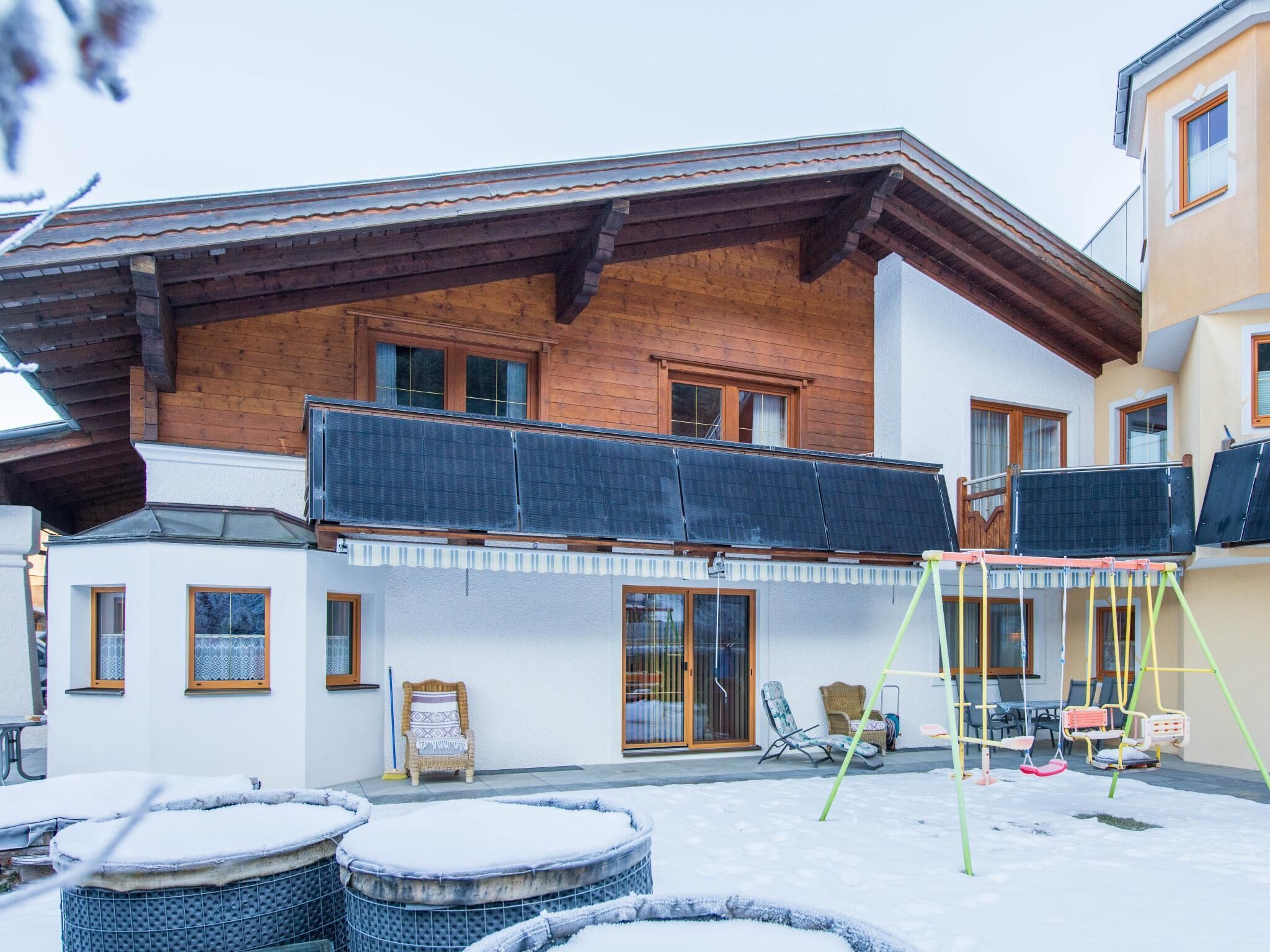 A two-story house with a wooden facade, a balcony, and a small patio area with a swing set.