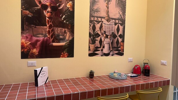 A wall with two artworks depicting giraffes, a tiled counter with chairs, and a small table with items. - Atelier 12 - by Be Your Home (Milano)